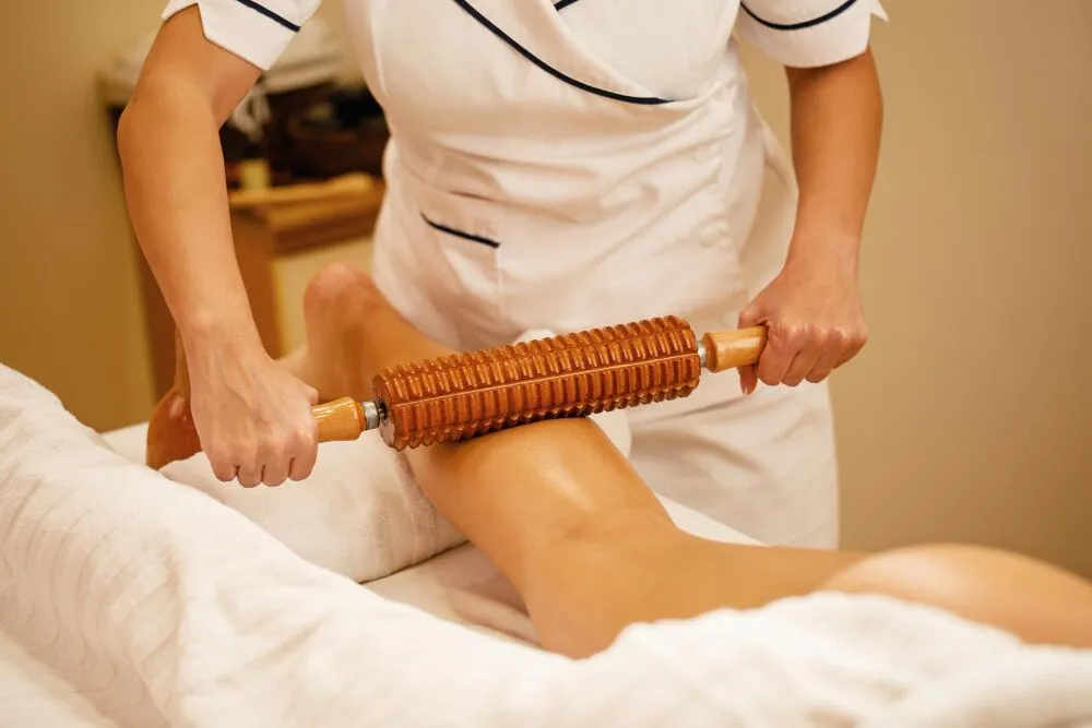 unrecognizable therapist performing maderotherapy womans legs during massage treatment spa